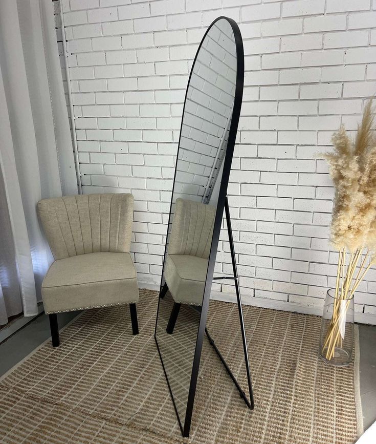Elongated freestanding mirror with black frame in a room with a chair and decorative elements.